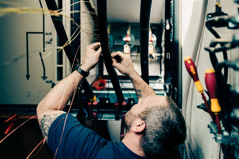 Ein Mitarbeiter der Stadtwerke arbeitet an einer Trafostation. Er ist von hinten zu sehen.